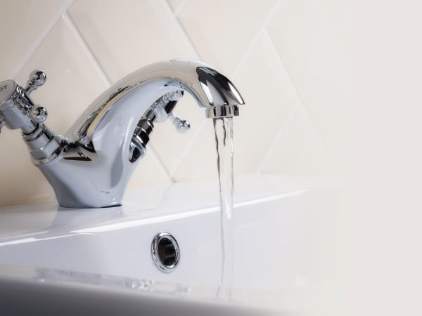 A closeup shot of water flowing from a basin mixer tap in the bathroom